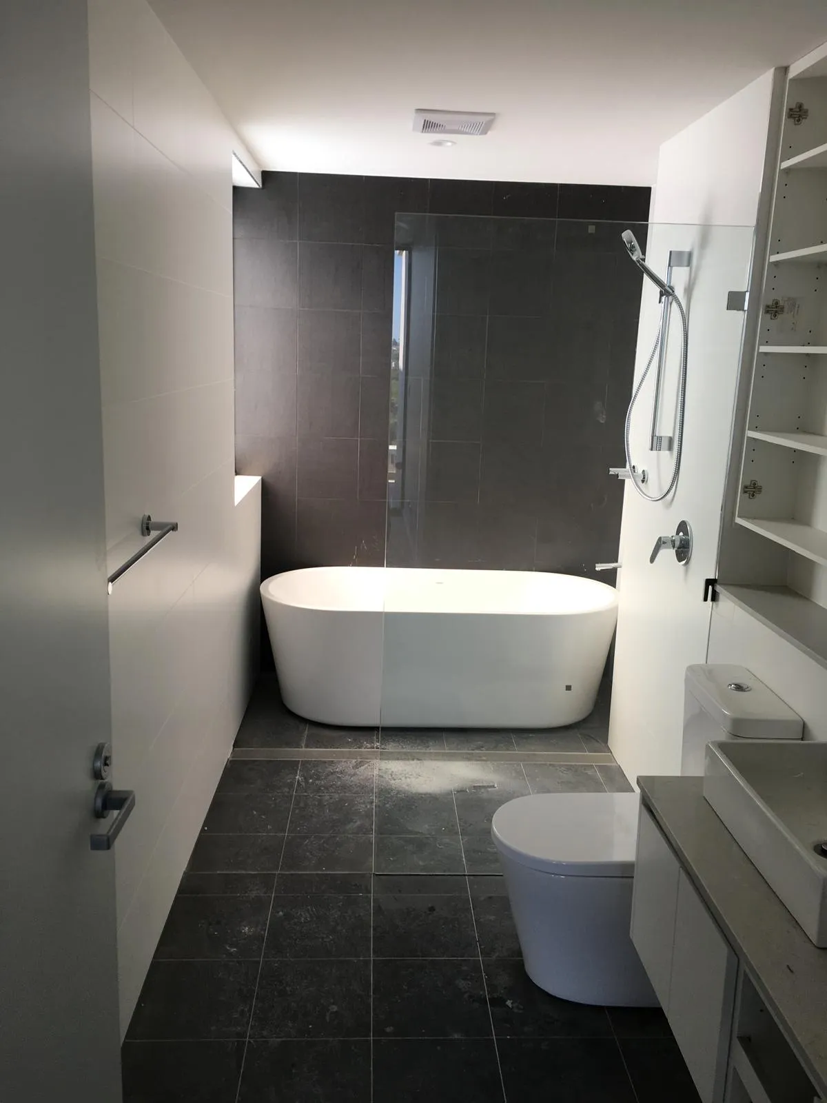 Bathroom with a charcoal tiled feature wall, freestanding bath and glass shower