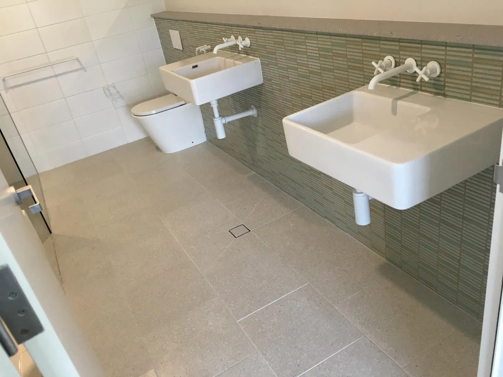 Bathroom with twin wall-mounted basins, sage green strip tiling and a concrete-look floor