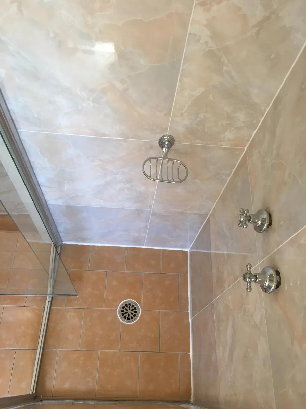 Shower corner finished in warm marble-look tiles with chrome tapware