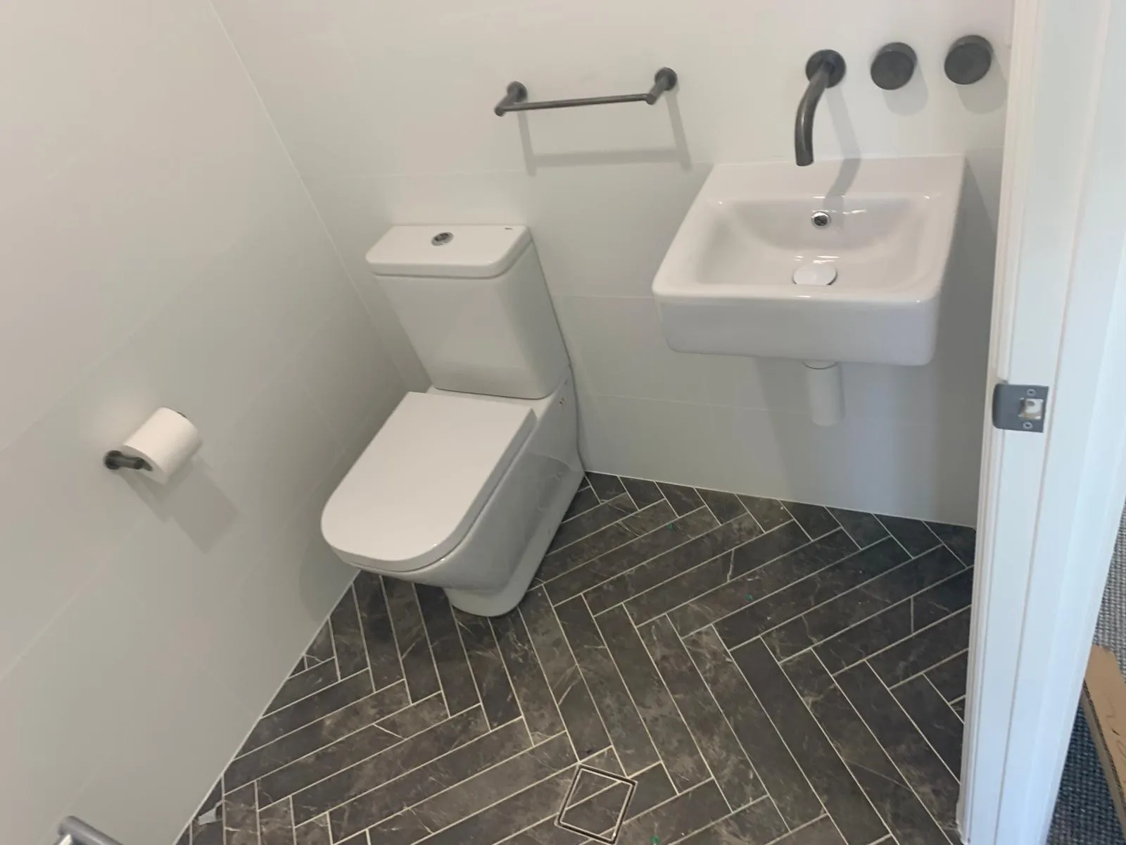 Powder room with a wall-mounted basin, matte black tapware and herringbone floor tiles