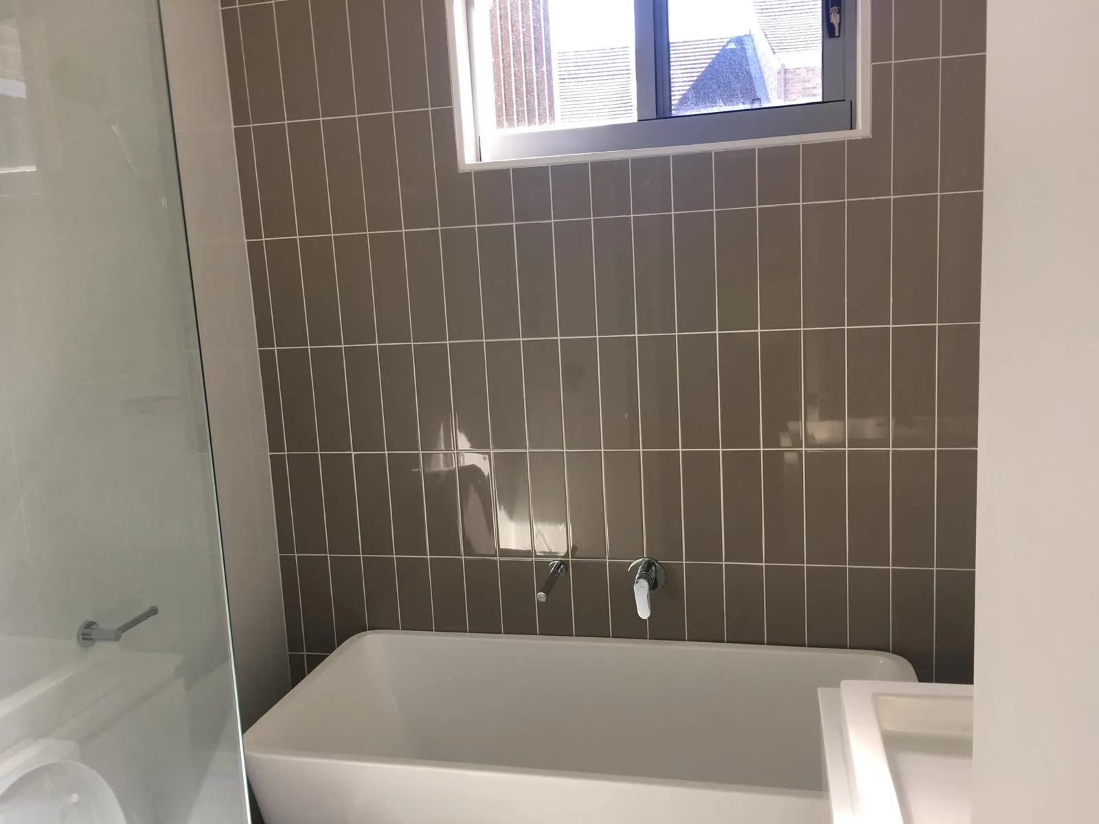 Bathroom with dark taupe vertical tiling and a freestanding bath below a window