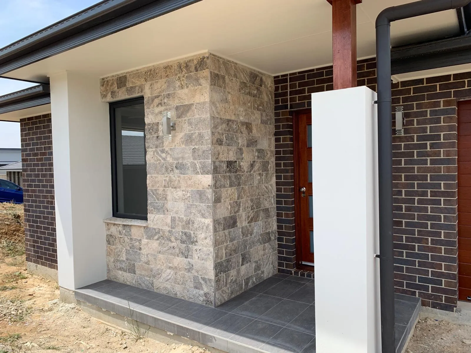 Home entry with stone cladding, dark brickwork and a timber front door