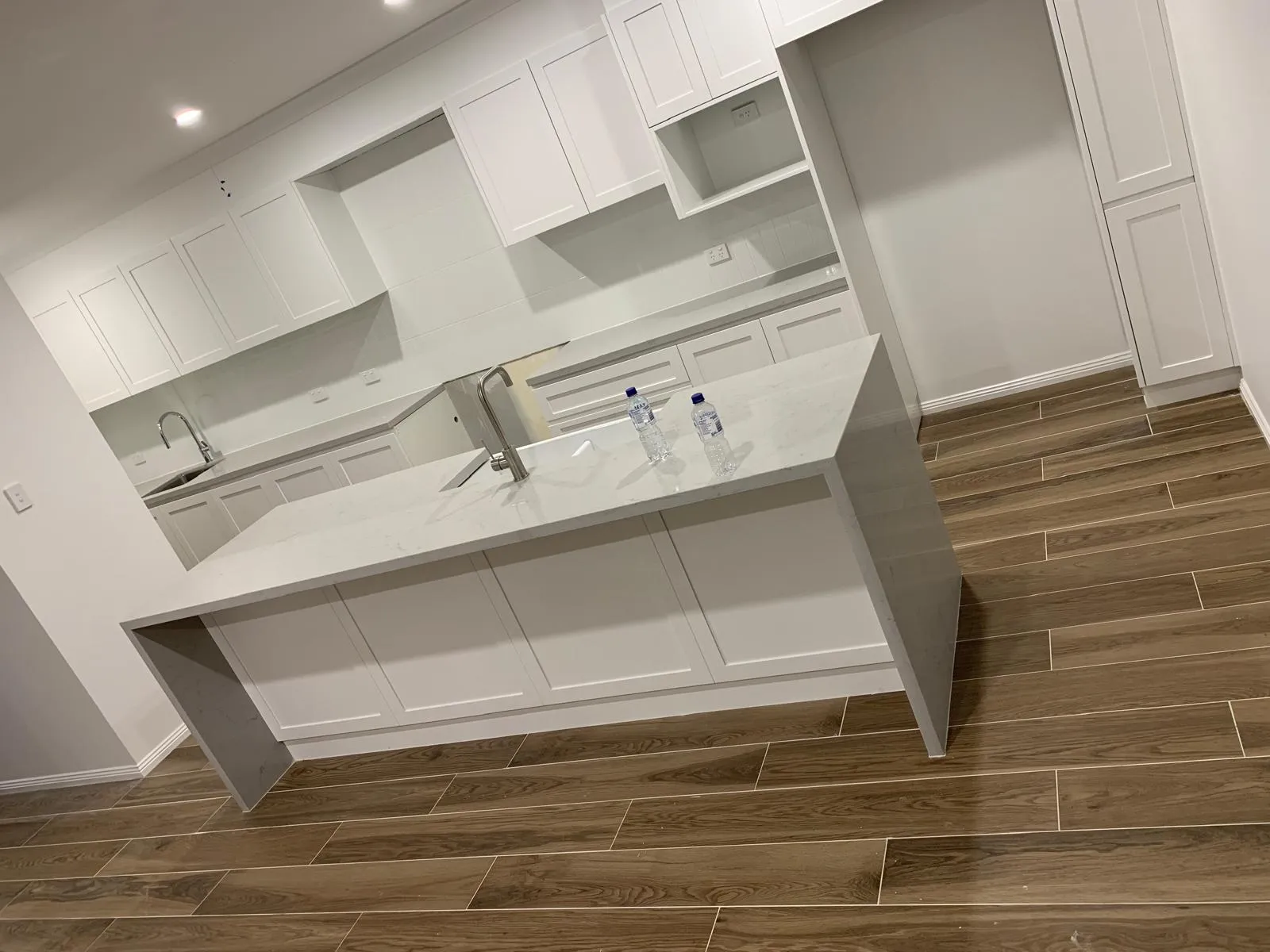 White shaker-style kitchen with a waterfall-edge stone island and wood-look plank flooring