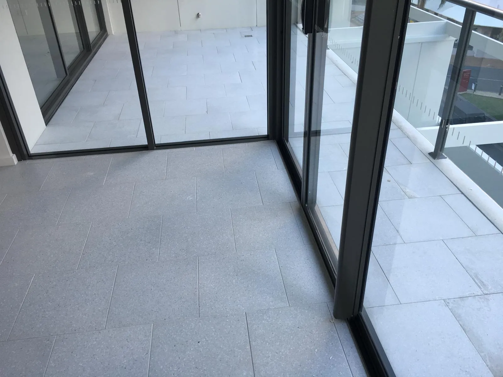 Terrace with pale grey terrazzo-look tiles, glass sliding doors and a glass balustrade