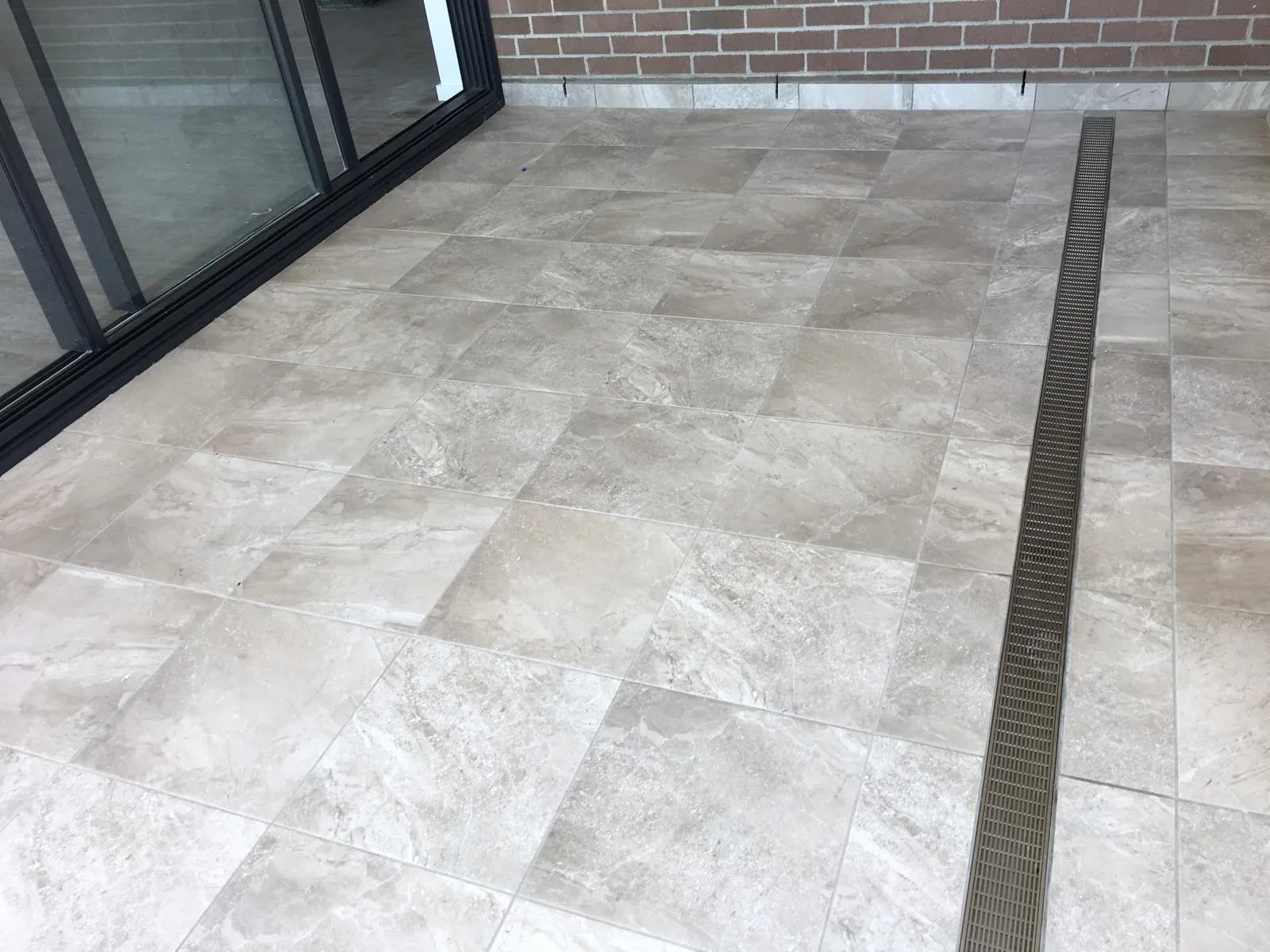 Outdoor terrace with pale stone-look tiles and glass balustrade